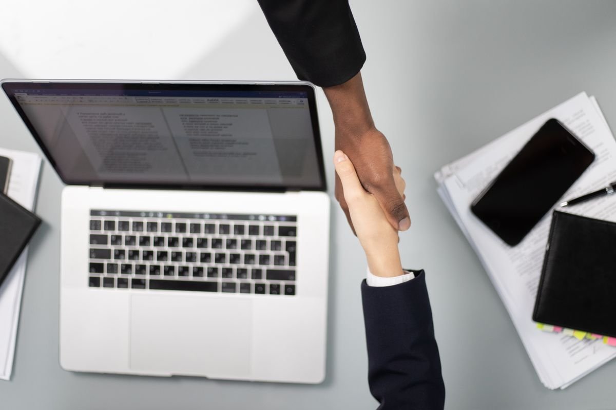Two website owners shaking hands over laptops, exchanging backlink partnership